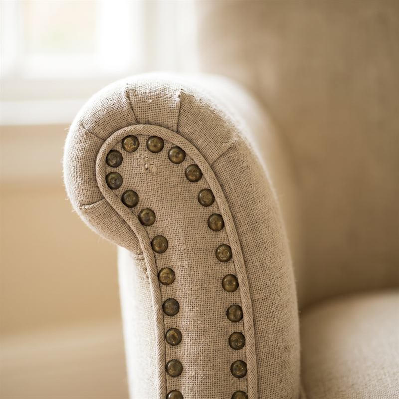 Détail d’un passepoil cousu main et d’une rangée de clous en laiton ancien sur l’accoudoir d’un fauteuil en lin